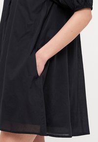 Μαύρο κοντό φόρεμα από ελαφρύ ύφασμα, με χαλαρή εφαρμογή και πλαϊνή τσέπη. Το στρίφωμα είναι ελαφρώς διαφανές με λεία υφή.