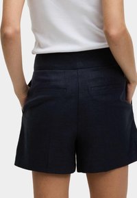 Granatowe szorty wykonane z textured tkaniny, z płaskim pasem, dwiema tylnymi kieszeniami i dopasowanym krojem, sięgające do połowy uda.