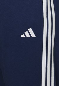 Malha de sweatshirt azul-marinho com um logótipo Adidas branco e três riscas brancas verticais de cada lado. Textura suave com um design ajustado.