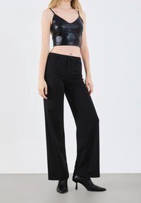 Black, fitted leather crop top with thin straps paired with high-waisted, loose black trousers and pointed black heels. Smooth textures throughout.