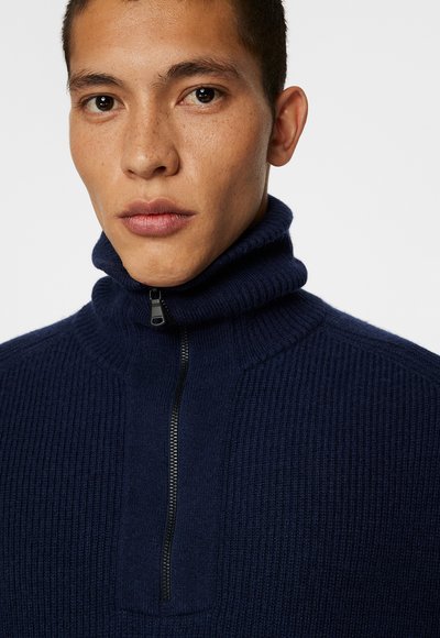 Marinblå ribbad zip-tröja med hög krage och svart dragkedjedetalj; strukturerad tyg med en snug passform runt nacken.