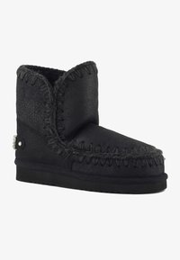 Botín negro de tobillo hecho de cuero texturizado con costuras en contraste y suela plana. Presenta un pequeño botón decorativo en el costado.