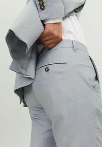 Helles blaues maßgeschneidertes Anzug mit einem glatten, strukturierten Stoff. Die Jacke hat einen detaillierten Ärmel und Knöpfe, während die Hose eine Gesäßtasche hat.