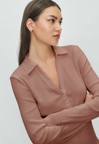 Polo a maniche lunghe di colore rosa in tessuto ribbed, con scollo a V e tre bottoni. Presenta un colletto strutturato e un design aderente.