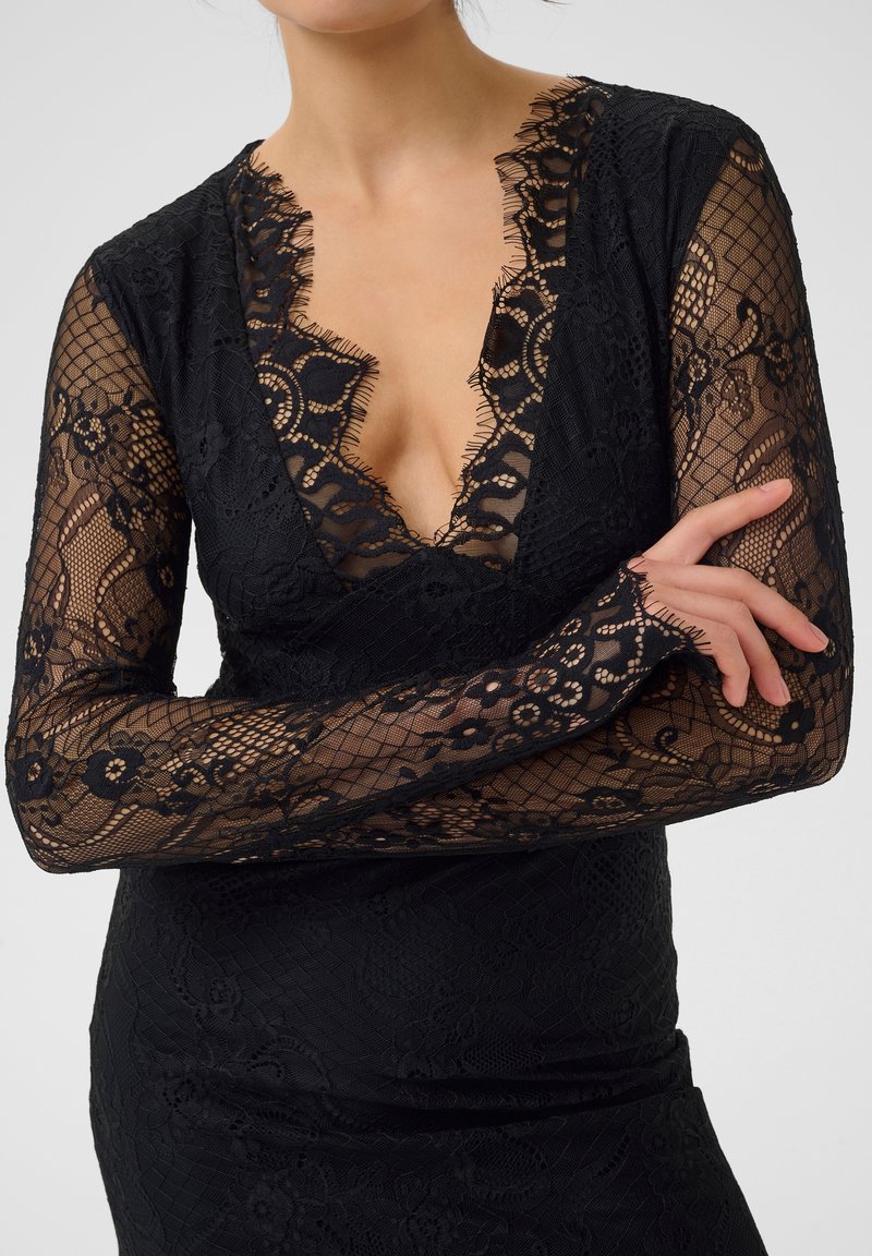 Robe en dentelle noire avec manches longues ornées de motifs floraux, décolleté en V profond, et tissu texturé avec des détails en transparence.