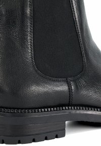 Zwarte leren Chelsea-boot met elastisch zijpaneel en dikke rubberen grof profielzool, close-up.