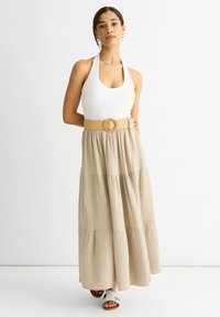 Top a fascia in tessuto bianco abbinato a una lunga gonna beige a più strati con un motivo testurizzato e una larga cintura di paglia con una fibbia circolare.