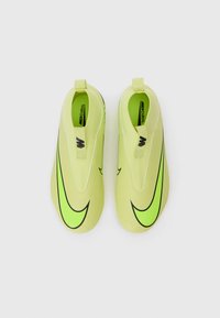 Jasnozielone, gładkie buty wsuwane z czarnym logo Nike i uchwytami ułatwiającymi zakładanie.