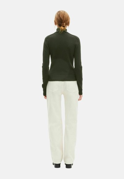 Suéter de cuello alto verde oscuro con textura acanalada, combinado con pantalones de pierna ancha en color blanco roto, mostrado desde atrás, destacando el ajuste y la silueta.