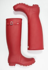 Bottes de pluie en caoutchouc rouges, montant jusqu'aux genoux, avec des semelles texturées, un détail en boucle argentée et une surface lisse. Présente un logo sur le côté extérieur.