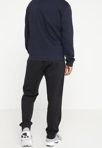Felpa blu navy con collo rotondo, polsini a costine e vestibilità comoda abbinata a pantaloni jogger neri con vita elasticizzata e orli risvoltabili.