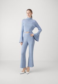 Lichtblauw geribbeld gebreid crop top met uitlopende mouwen, gecombineerd met bijpassende uitlopende broeken. Witte puntige hakken maken de outfit compleet.