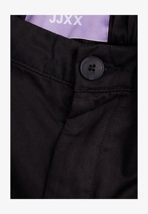 Schwarze Stoffhosen mit einem schwarzen Knopfverschluss, sichtbaren Nähdetails und einem lila Etikett mit der Aufschrift "JJXX."