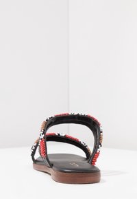 Svart sandal med två breda remmar prydda med röda, vita och svarta pärlor. Har en platt sula och en jämn lädertextur.