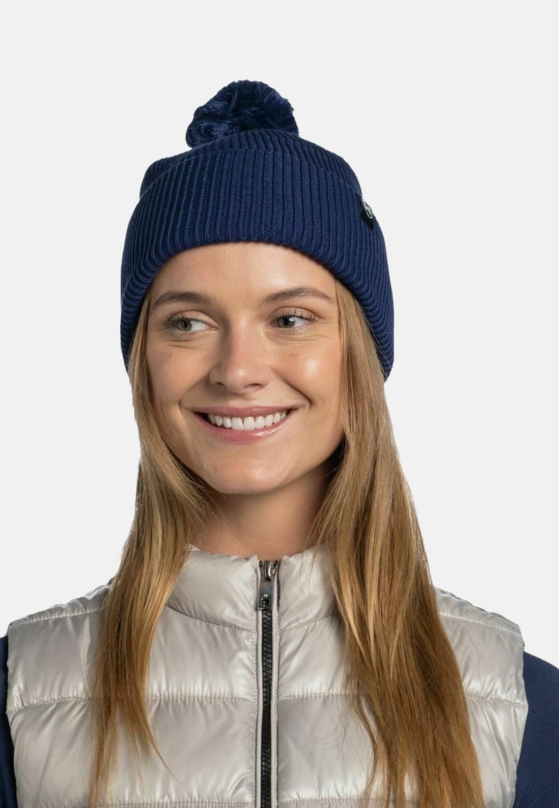 Navy knitted beanie with a ribbed texture and a pom-pom on top, paired with a silver puffer vest featuring a zip front.
