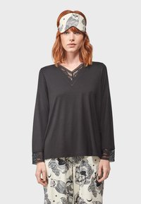 Haut noir à manches longues avec des accents en dentelle au niveau du col et des poignets, associé à un pantalon crème orné d'un motif de hibou et de fleurs.