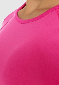 Maglietta sportiva aderente di un vivace colore rosa, con scollo rotondo e tessuto morbido e elasticizzato, caratterizzata da dettagli cuciti lungo le spalle.