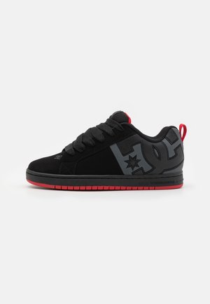 Schwarzer und roter Sneaker mit niedrigem Schnitt, dicken Schnürsenkeln, großem grauem Logo an der Seite und rotem Zuglasche an der Ferse, seitlich auf weißem Hintergrund gezeigt.