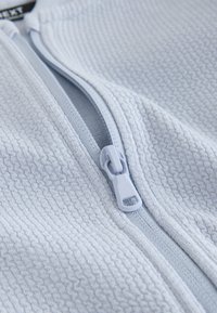 Light gray textured fabric with a partially open matching zipper and pull tab in close-up view.