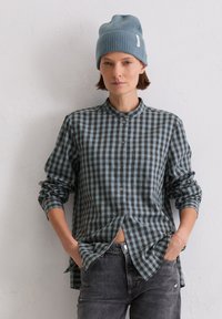 Plaid button-up shirt in dark blue and green, soft fabric, and rounded collar. Worn with gray jeans and a light blue knit beanie.