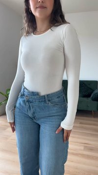 Blusa de manga longa branca feita de um tecido suave, combinada com jeans de cintura alta azuis claros. Apresenta um decote redondo e mangas justas.