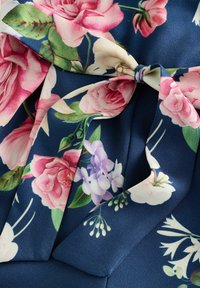 Tessuto floreale con grandi rose rosa e fiori viola più piccoli, su uno sfondo blu navy. Texture morbida e liscia con un dettaglio annodato.