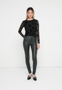 Sort langærmet top med blomsterbroderi, parret med tætsiddende mørke grå faux læderbukser og spidse sorte flade sko. Enkel, strømlinet design.