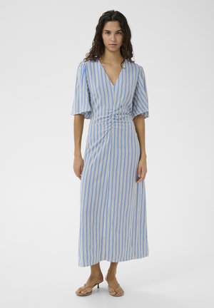 Kvinde iført en lang kjole med blå, gule og hvide lodrette striber, med indsnøring i taljen og albuelange ærmer, stående på en hvid baggrund.