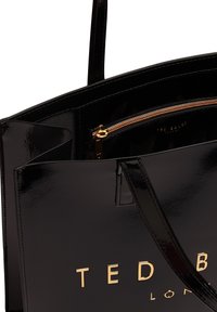 Τσάντα tote από μαύρο δερμάτινο λάστιχο με χρυσά μεταλλικά στοιχεία. Διαθέτει τσέπη με φερμουάρ και ανάγλυφο λογότυπο. Λείο υφή και δομημένο σχήμα.