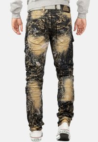 Pantaloni cargo in stile camouflage con un mix di motivi neri, beige e bianchi, cinque tasche e vestibilità slim; tessuto testurizzato con cuciture visibili.