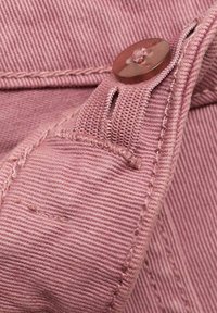 Roza tekstil z rebrasto teksturo, ki se zapira z gumbom in ima ob strani tkan trak. Vidne šive ob sklepih.