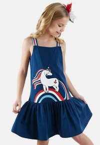 Marineblaues ärmelloses Kleid mit einem rüschierten Saum, das eine weiße Einhorngrafik und mehrfarbige Regenbogenakzente auf einem einfarbigen Hintergrund zeigt.