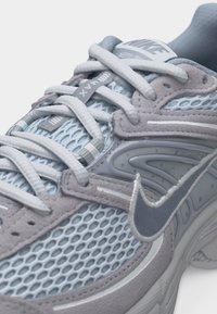 Hallkaader halli ja helesinise Nike Air Max tennisejalatsist, kus on näha võrkriie, seemisnahast detailid, paelad ja Nike viirglogo.