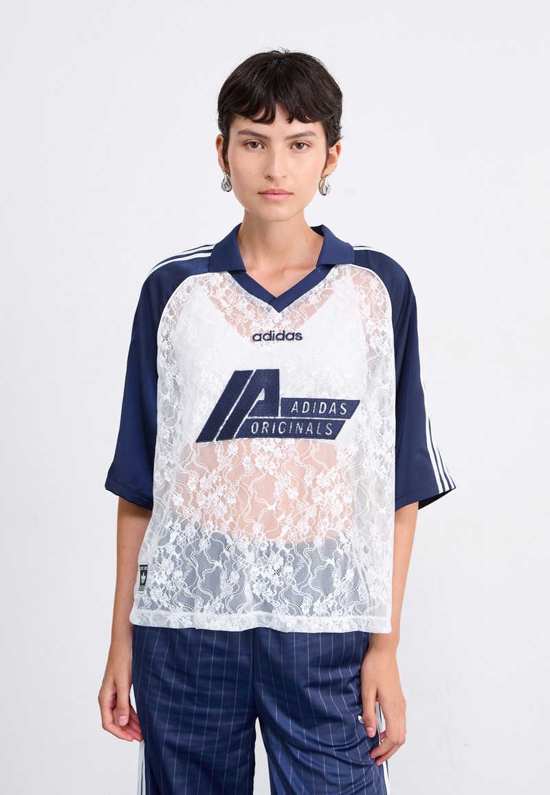 Balta džersija ar mežģīņu pārklājumu un tumši zilu apkakli un piedurknēm, ar lielu tumši zilu Adidas logotipu. Brīva forma ar sānu svītrām.