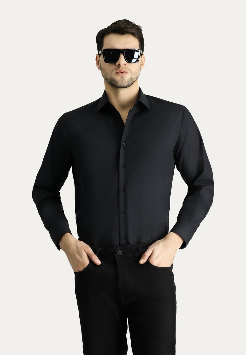 Camicia nera a maniche lunghe realizzata in tessuto liscio, con bottone frontale, colletto e una singola tasca sul petto, abbinata a pantaloni neri.