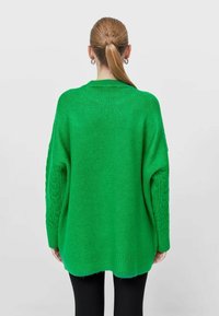Pull en maille vert oversize avec manches à torsades et ourlet côtelé. Texture douce et coupe décontractée, présenté en vue arrière.
