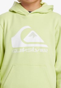 Hoodie verde chiaro realizzato in tessuto morbido, con un logo grafico bianco e una tasca frontale. Il design include un cappuccio regolabile con cordino.