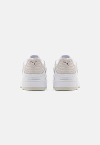 Hvide lædersneakers med beige ruskindsdetaljer, teksturerede elementer på hælen og en gummisål. Har signaturlogoet på bagsiden.
