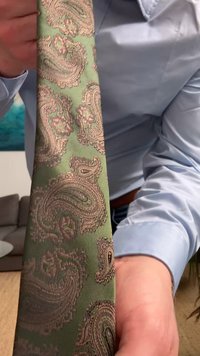 Grønn paisley slips med intrikate mønstre i nyanser av beige og brunt, laget av glatt stoff med en subtil glans og myk tekstur.