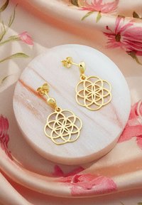 Orecchini d'oro con un design a motivo floreale ritagliato, con una finitura lucida e chiusura a perno, esposti su una superficie rotonda in marmo.
