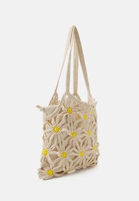 Gehaakte tote bag in beige met bloemenontwerp; heeft gele bloemaccenten, dubbele gevlochten hengsels en een zachte stoffen binnenkant.