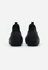 Black slip-on shoes with a textured finish, featuring a round toe, high back, and pull tab for easy wear. Minimalist design with branding at the heel.