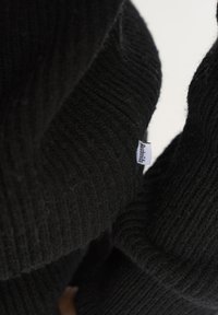 Sort strikket sweater med ribbet tekstur og lille stofmærke. Materialet ser blødt og varmt ud, velegnet til koldt vejr.