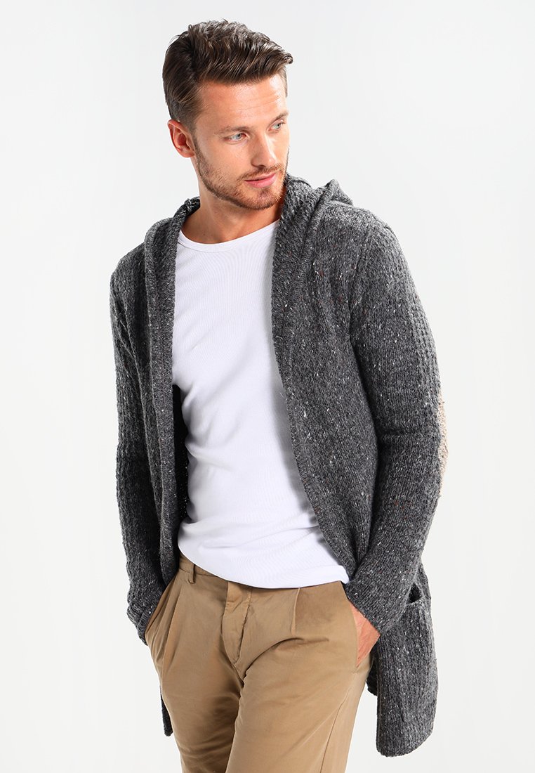 Cárdigan gris de punto con capucha, que presenta un patrón texturizado y un diseño de frente abierto; combinado con una camisa blanca y pantalones beige.