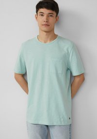 Licht mintgroene t-shirt gemaakt van een zachte stof, met een ronde hals en een enkele borstzak. Het ontwerp heeft korte mouwen en een relaxte pasvorm.