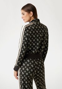 Black tracksuit with intricate silver patterns, including logos, featuring a high collar, side stripes, and ribbed cuffs.