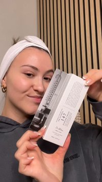 Hvid boks med sort tekst, prydet med et grafisk design af en spiral. Personen holder den til venstre og har en grå hættetrøje og et hvidt pandebånd på.