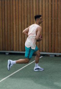 Sportlik riietus, kus on hele roosa ilma varrukateta topp ja türkiissinised lühikesed püksid mustade triipudega. Jooksmine väljakul. Valged spordijalatsid.