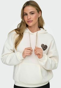 Hvit hettegenser laget av mykt stoff, med en leopardmønstrede hjerteapplikasjon på venstre side, med snorer og en frontlomme.