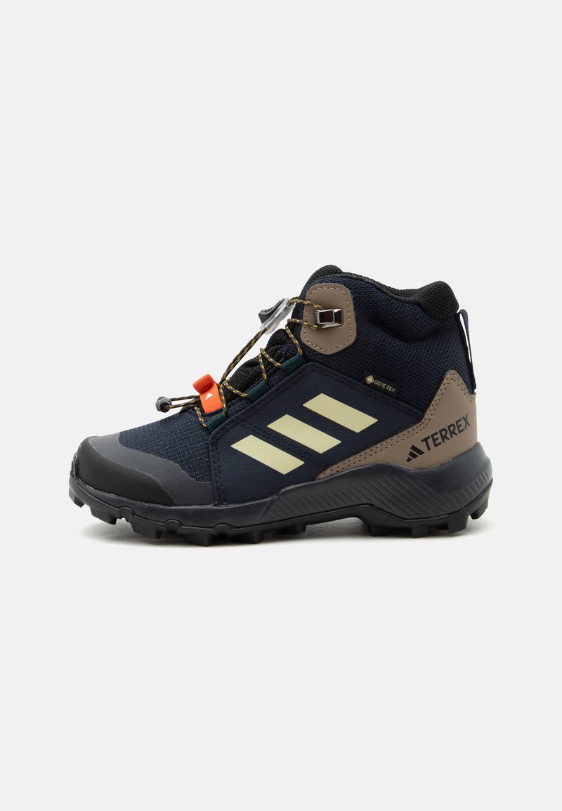 Μαύρο και καφέ μποτάκι πεζοπορίας Adidas Terrex με παχιά σόλα, μπεζ ρίγες, ετικέτα Gore-Tex και πορτοκαλί κλείδωμα κορδονιών σε λευκό φόντο.